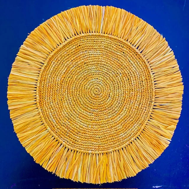 Top-down view of a Soleil Fringe marigold raffia placemat, featuring a feathered sun-ray fringe border and soft matte handwoven texture for a bohemian tablescape.