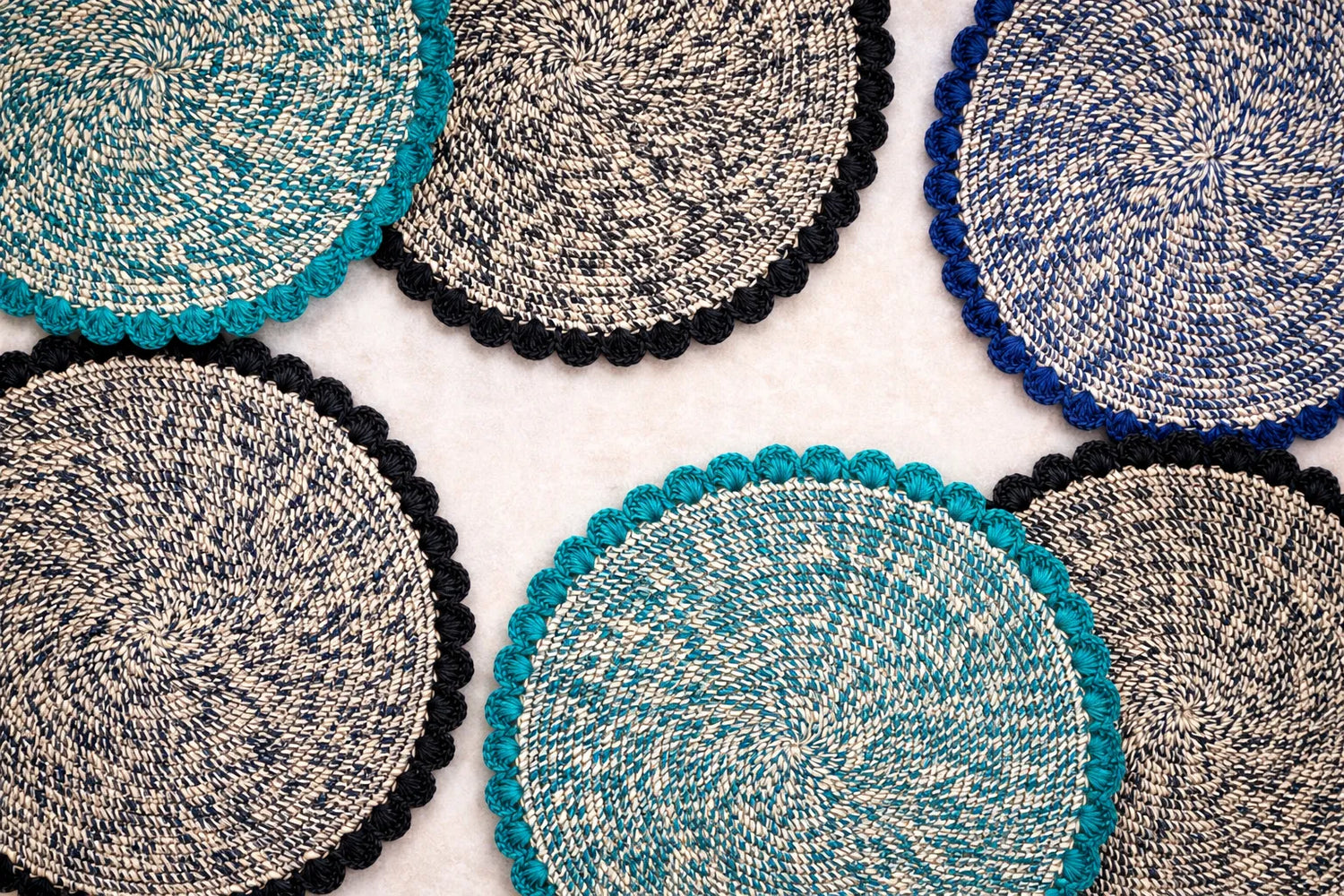 A group of handwoven raffia charger plates from the Speckled Collection featuring elegant scalloped edges and earthy mottled textures.