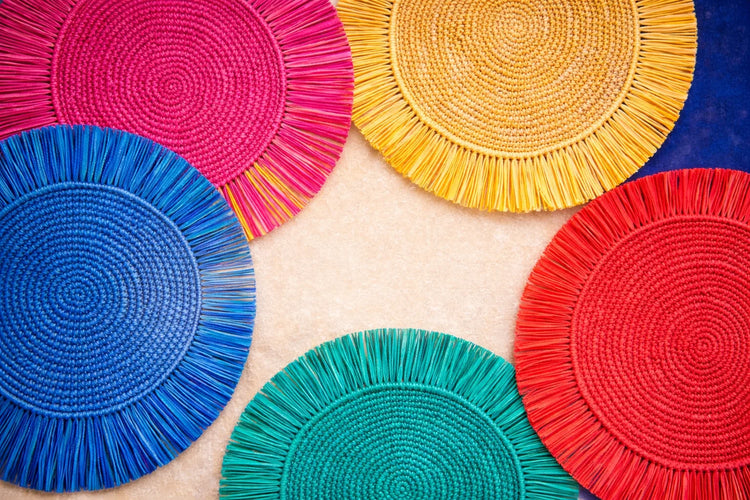 A colorful variety of Soleil Fringe handwoven rattan charger plates in bohemian styles.