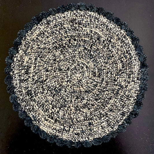 Top-down view of an Onyx Speckle hand-crocheted raffia placemat, showcasing the charcoal black multi-tonal weave and soft scalloped edges for a modern tablescape.