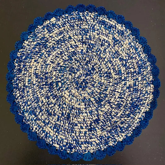 Top-down view of a Sapphire Speckle hand-crocheted raffia placemat, showcasing the soft indigo blue weave and artisanal scalloped edges for a coastal dining table.