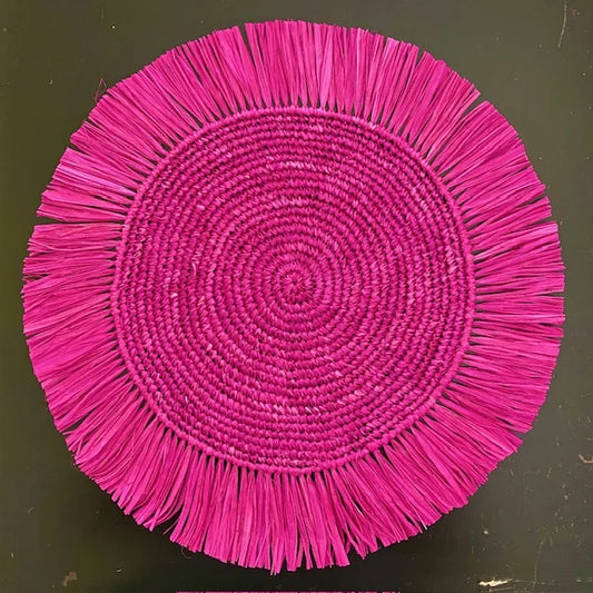 Top-down view of a Soleil Fringe hibiscus pink raffia placemat, showing the radiant tropical fuchsia fringe border and soft handwoven texture for a preppy-coastal table.