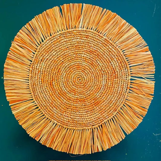 Top-down view of a Soleil Fringe sunset orange raffia placemat, showing the radiant warm amber fringe border and soft handwoven texture for a Mediterranean-style table.