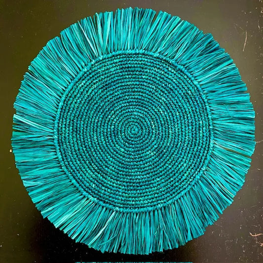 Top-down view of a Soleil Fringe peacock teal raffia placemat, showing the radiant jewel-toned fringe border and soft handwoven texture for a botanical-themed table.