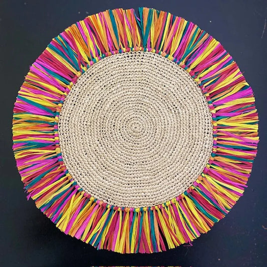 Close-up of a Soleil Fringe rainbow raffia placemat, showcasing the vibrant multi-colored weave and feathered fringe border for a festive, sun-drenched tablescape.