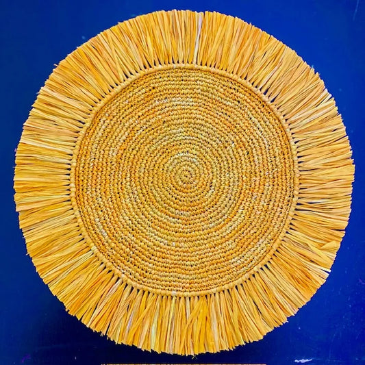 Top-down view of a Soleil Fringe marigold raffia placemat, featuring a feathered sun-ray fringe border and soft matte handwoven texture for a bohemian tablescape.